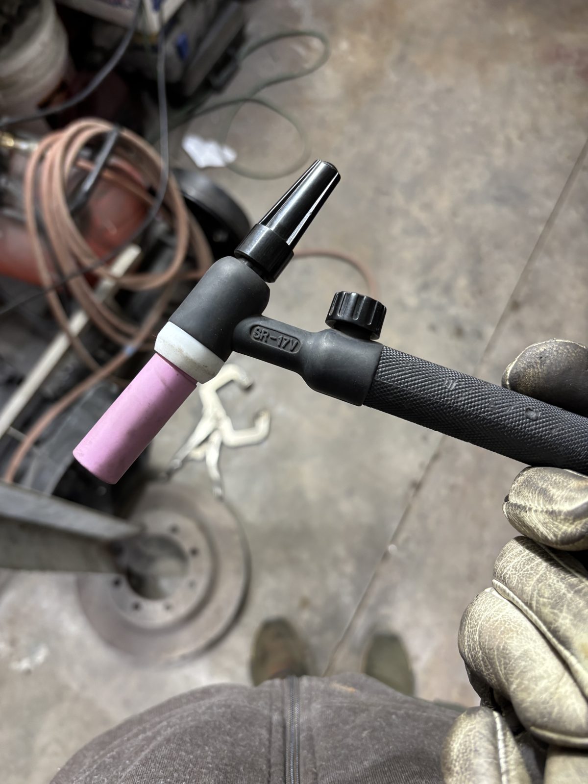 Gloved hand holding a TIG torch with a pink ceramic cup